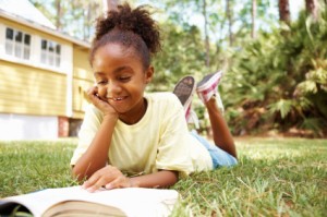 Picture of a child reading a book on the grass.