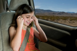 Keeping Kids Entertained on Road Trips, Photo of a child with earphones on in the back seat of a car.