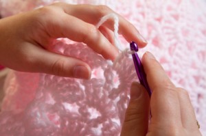 A person crocheting a pink baby blanket.