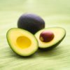 Two avocados, one cut in half with the seed inside.