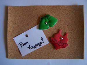 Green Shorts and Red Swimsuit attached to Cork Board with Brads. White note has Bon Voyage! written on it.