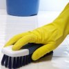 Gloved hand scrubbing a tile floor with a brush.