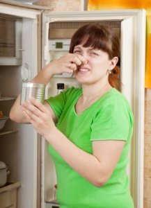 Photo of a woman holding her nose in front of her refrigerator.