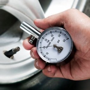 Checking Your Vehicle's Tire Pressure, Man holding a tire gauge, with tire in background.