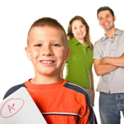 Young Boy Holding Up A+ Paper in Front of Proud Parents