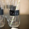 Tall Glasses with black stripe of chalkboard painted on them. The glass centered inthe image has Kate written on it, a yellow striped straw in the glass and a piece of chalk laying in front. 