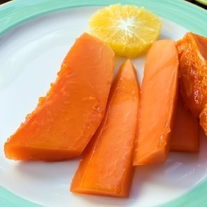 Slices of peeled papaya on a plate with an orange slice.