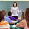 A teacher at the front of a classroom, in front of a chalkboard.