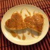 Two heart shaped pancakse on a plate with syrup drizzled over them