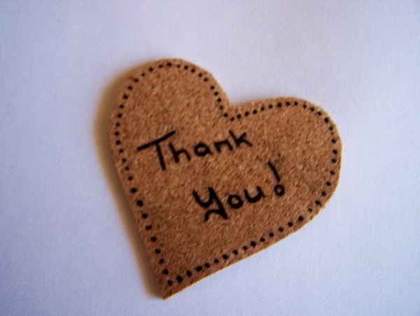 cork cut into the shape of a heart with the wrods Thank you! written diagonally across the center in black and small black dots outlining the edges of the heart