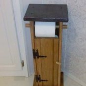 A bathroom toilet paper holder that is built like an outhouse.