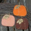 Three pumpkins against a branch wreath and weather wooden fence.