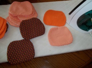 Several pumpkin shapes after sewing and turning. They are scattered on an ironing pad next to a steam iron.