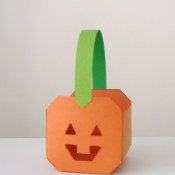Small paper paper pumpkin basket. Pumpkin is orange, handle is green.