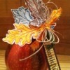 Speckled pumpkin or gourd with paper leaves, acorn, and raffia decorations. 