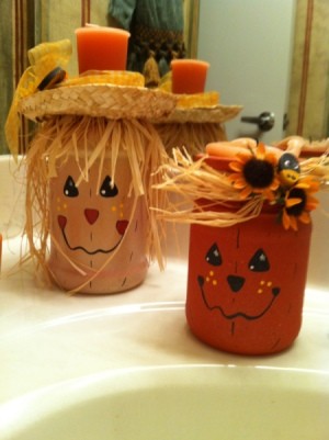 A scarecrow and a pumkin candle holder sitting on a sink.