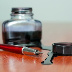Spilled ink on wood surface. There is also an open bottle and a pen.