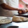 Tortilla on a grill with man rolling torillas in the background