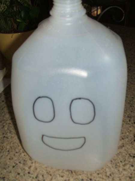 White one gallon milk jug with two round eyes and a mouth drawn on.