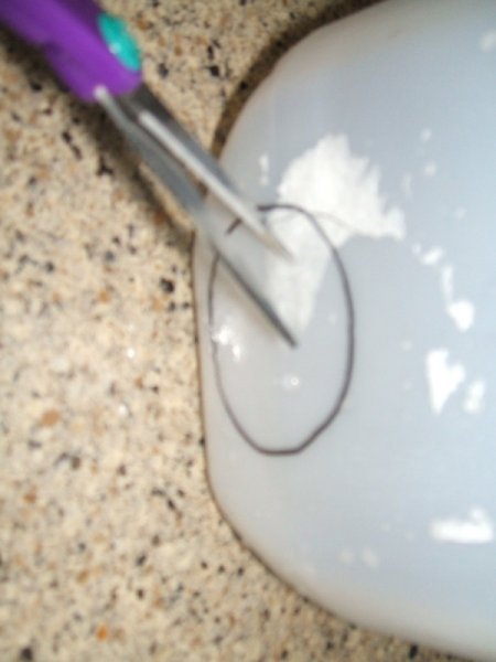 Scissors cutting hole for votive in the bottom of the milk jug.