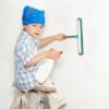 Young boy sitting on a step ladder cleaning a wall.