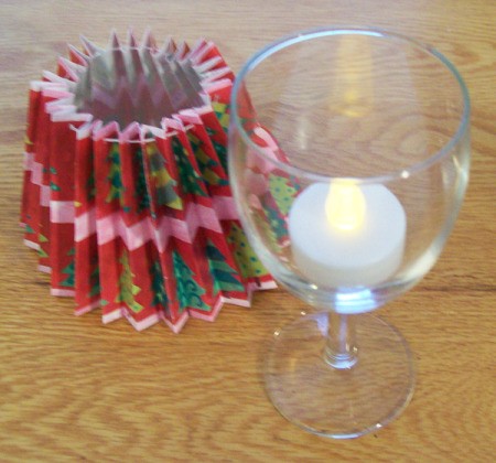 Glass with tea light inside and shade next to in on table.