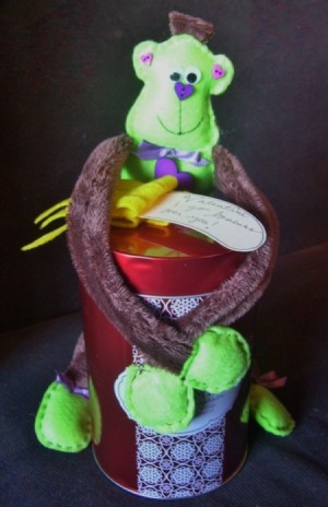 Green monkey wrapped around a red can, holding card.