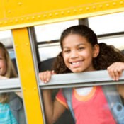 Two kids smiling out a school bus window.