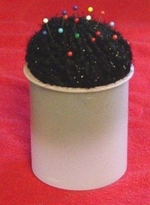 Pincushion made from frosting tub and ball of yarn.
