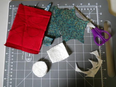 Sewing grid board with cut out leaves, circles of batting for berries and a pair of scissors.
