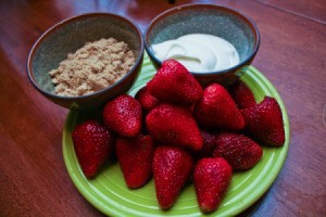 A plate of strawberries with bowls of sour cream and brown sugar.