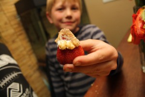 A blond boy holding a strawberry dipped in sour cream and brown sugar