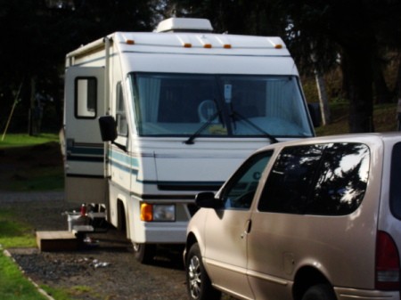 An RV with a minivan in front, at a campsite.