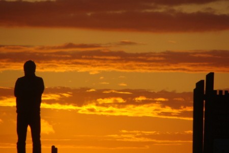 A vivid Oregon coast sunset with a silhouette of a man to the left.