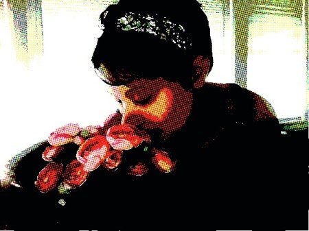 A dark haired woman smelling red roses.