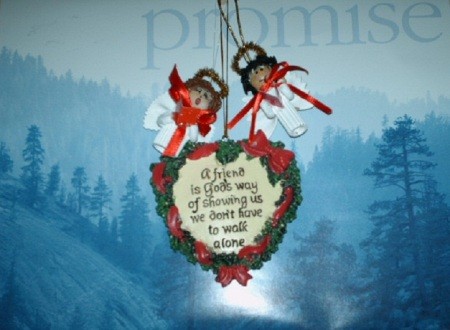 A heart shaped Christmas ornament hanging with two noodle angels over a calendar that says "Promise".