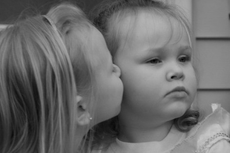 A black and white photo of two young sisters, one kissing the cheek of the other.