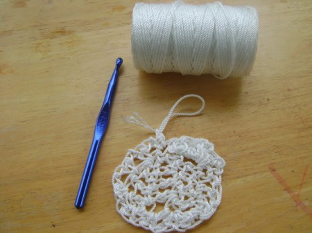 white crocheted pot scrubber, spool of nylon string, and crochet hook