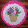 Pink circular card with basket of flowers on white doiley.