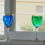 A close up of two wine glasses in a window filled with colored water
