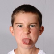 A boy making a mean face and sticking out his tongue.