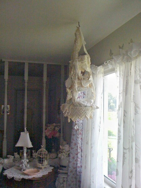 A lace chandelier in front of a window with sheer curtains.
