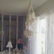 A lace chandelier in front of a window with sheer curtains.