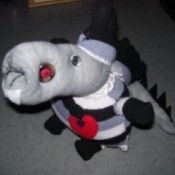 Cute long snouted creature made from a gray, black, and white striped sock. It has a spiky tail and a red bottle cap hanging around its neck.