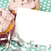 A paper invitation leaning up against two cupcakes.