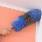 Someone dusting the corner of a room with a duster.