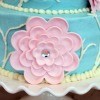 close up of a pink gumpaste flower with a rhinestone center on a teal cake siting on a cake stand