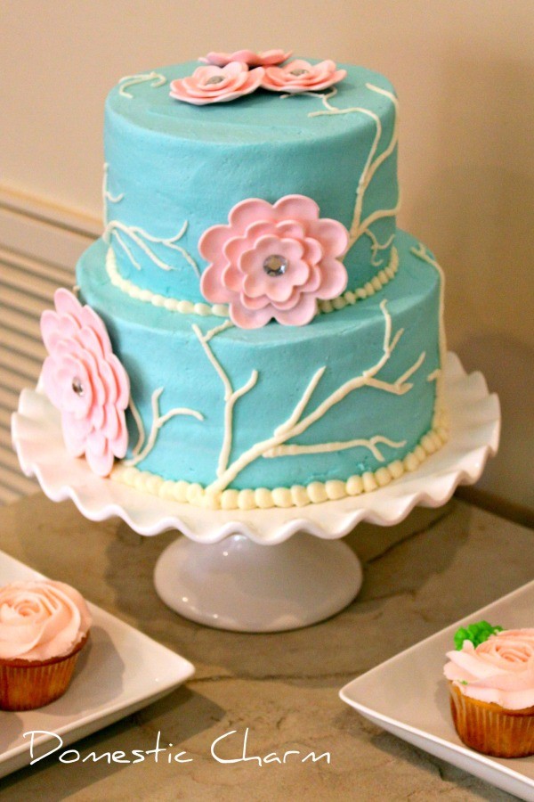 tiered teal cake with pink gumpase flowers on a cake stand