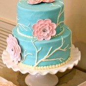 tiered teal cake with pink gumpase flowers on a cake stand