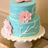tiered teal cake with pink gumpase flowers on a cake stand